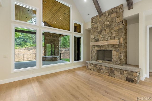 unfurnished living room featuring high vaulted ceiling, a stone fireplace, and light wood-type flooring