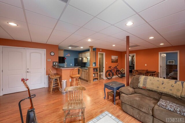 living room featuring light wood-type flooring, a drop ceiling, and bar area