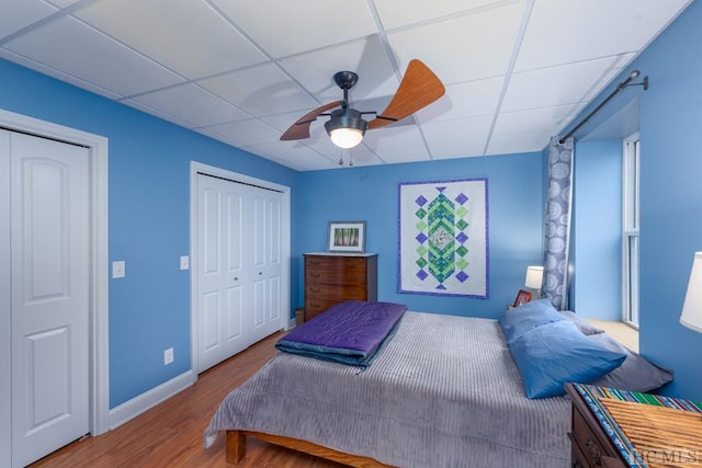 bedroom with a drop ceiling, wood-type flooring, and ceiling fan