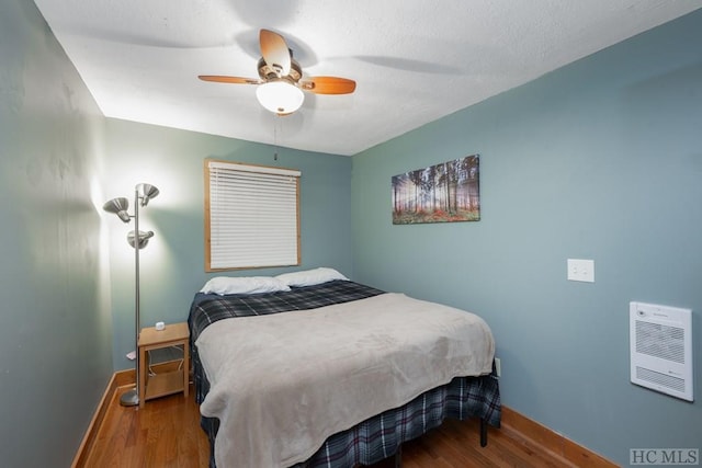 bedroom with wood-type flooring, heating unit, and ceiling fan