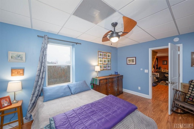 bedroom with ceiling fan, a drop ceiling, and wood-type flooring