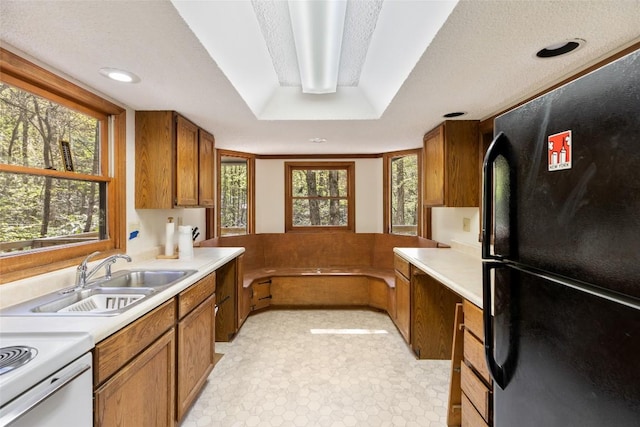 kitchen with freestanding refrigerator, brown cabinetry, a sink, and light countertops
