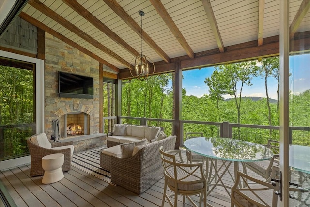 sunroom / solarium with outdoor dining area, a notable chandelier, an outdoor living space with a fireplace, and beam ceiling