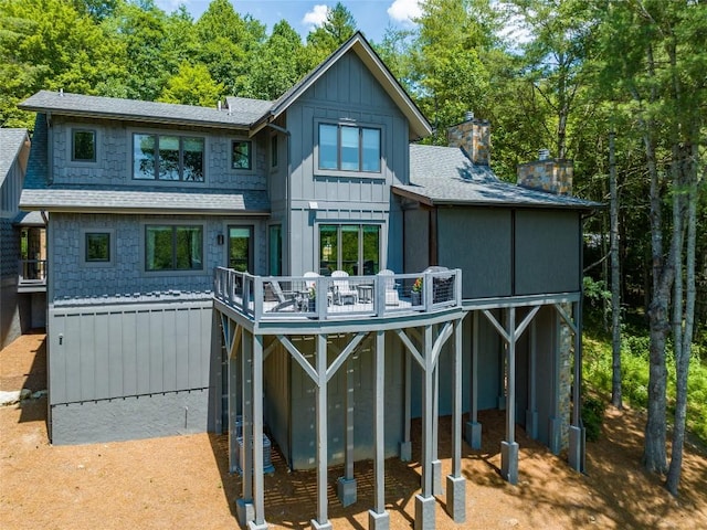 back of house featuring board and batten siding, a deck, a shingled roof, and a chimney