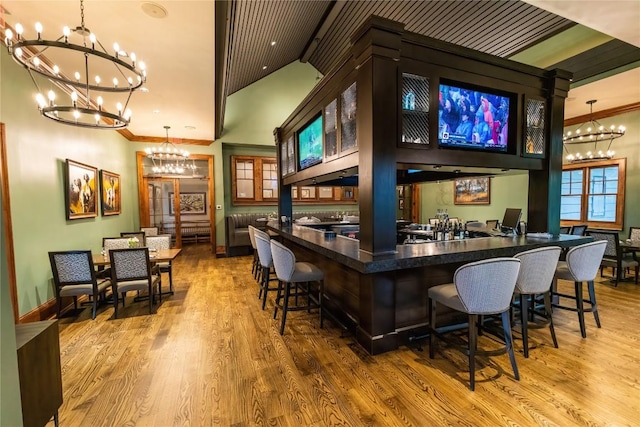 bar with ornamental molding, wood finished floors, vaulted ceiling with beams, a notable chandelier, and decorative light fixtures