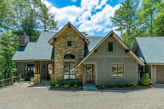 view of front facade featuring board and batten siding, a shingled roof, stone siding, and a chimney