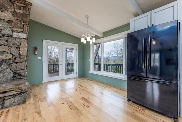 unfurnished dining area with lofted ceiling with beams, light wood-style floors, a notable chandelier, and french doors