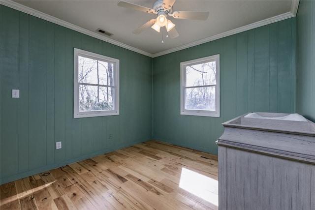 unfurnished room featuring a wealth of natural light, light wood finished floors, ornamental molding, and visible vents