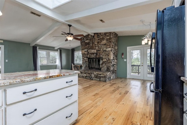 kitchen with visible vents, freestanding refrigerator, white cabinets, light wood-type flooring, and vaulted ceiling with skylight