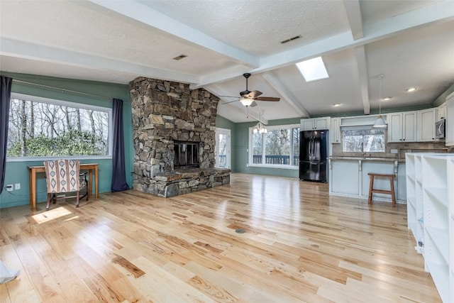 unfurnished living room with a textured ceiling, vaulted ceiling with skylight, a fireplace, visible vents, and light wood-style floors