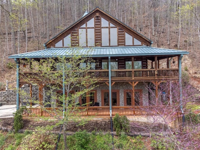 view of front facade featuring a deck, a wooded view, stone siding, metal roof, and a standing seam roof