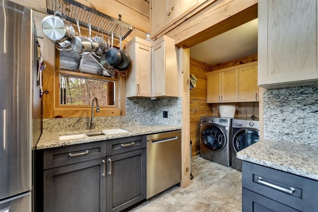 kitchen with light stone countertops, a sink, stainless steel appliances, backsplash, and washing machine and dryer