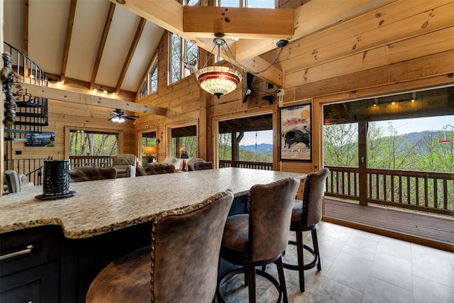 interior space featuring light tile patterned floors, a ceiling fan, beam ceiling, wood walls, and high vaulted ceiling