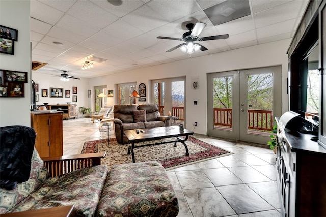 living room featuring light tile patterned flooring, french doors, ceiling fan, and a drop ceiling