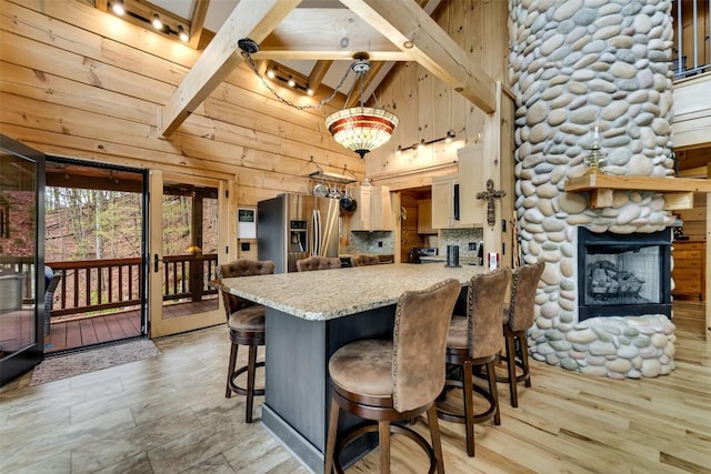 kitchen featuring stainless steel fridge with ice dispenser, a peninsula, a fireplace, high vaulted ceiling, and a breakfast bar area