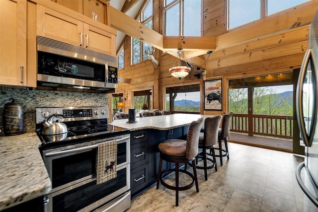kitchen with tasteful backsplash, a towering ceiling, wooden walls, a healthy amount of sunlight, and appliances with stainless steel finishes