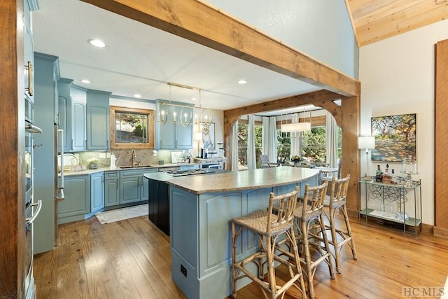 kitchen with blue cabinetry, decorative backsplash, light wood-style floors, a sink, and a kitchen island