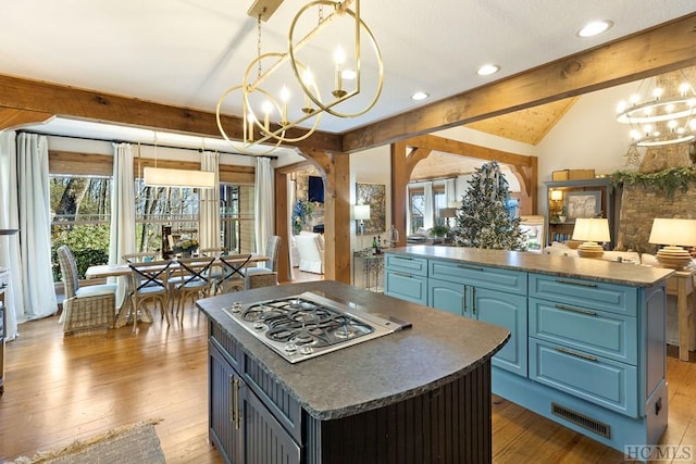 kitchen with blue cabinets, stainless steel gas cooktop, dark countertops, a kitchen island, and a chandelier