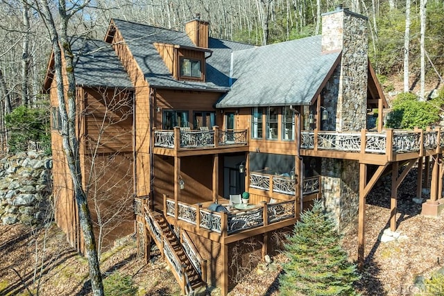 rear view of house with a shingled roof, stone siding, a chimney, stairway, and a wooden deck