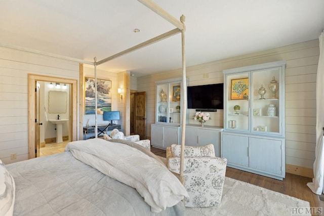 bedroom featuring a sink, connected bathroom, wooden walls, and wood finished floors