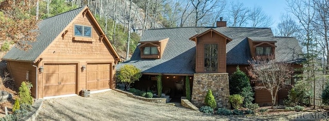 view of front of house with an outbuilding, stone siding, a chimney, and a garage