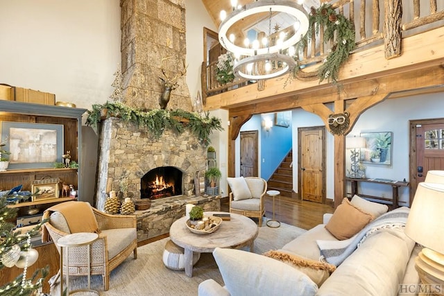 living area featuring stairway, a towering ceiling, an inviting chandelier, a stone fireplace, and wood finished floors