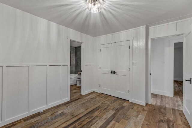 453 Bright Mountain Rd, Cullowhee, NC 28723 - unfurnished bedroom featuring wood finished floors, a chandelier, a closet, ensuite bathroom, and wainscoting