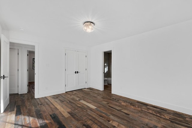 unfurnished bedroom featuring ensuite bathroom, dark wood-type flooring, and a closet