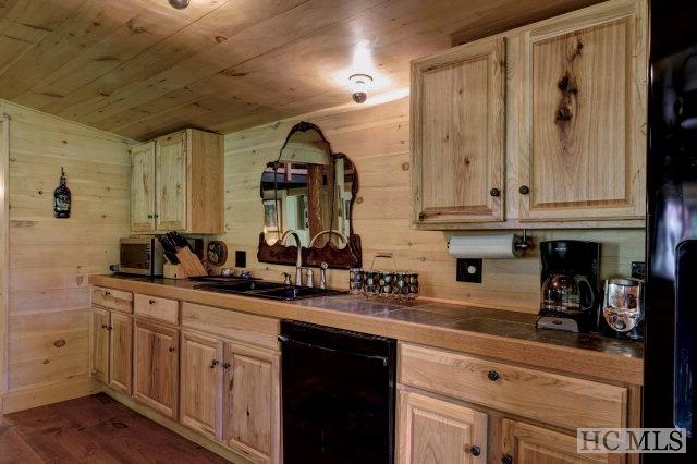 kitchen with wood ceiling, black dishwasher, light brown cabinets, sink, and wooden walls