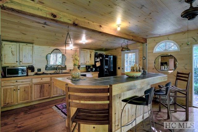 kitchen featuring a breakfast bar area, wooden walls, light brown cabinets, black fridge, and dark hardwood / wood-style floors