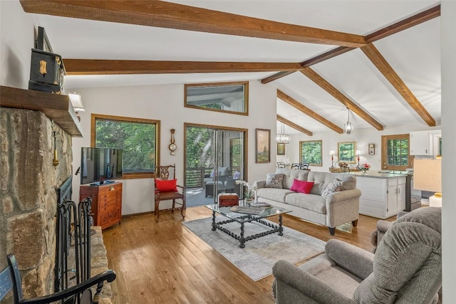 living room featuring lofted ceiling with beams, light wood-type flooring, and a stone fireplace