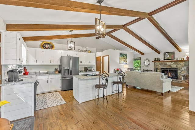 kitchen with light wood finished floors, a kitchen bar, appliances with stainless steel finishes, a fireplace, and white cabinets