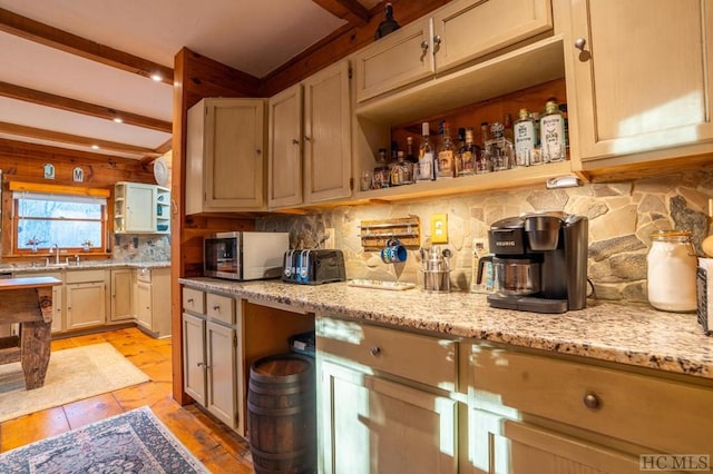 kitchen featuring light stone counters, backsplash, sink, and beamed ceiling