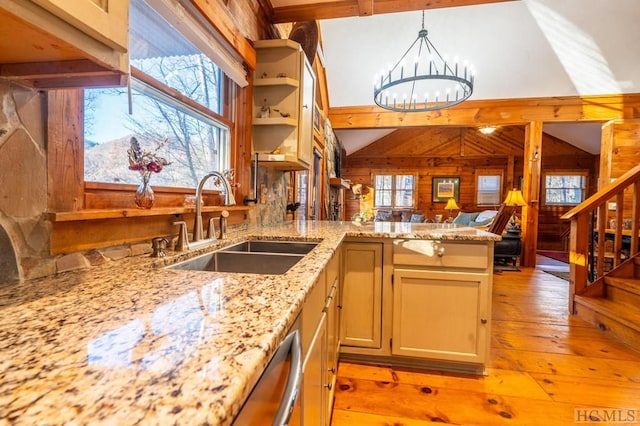 kitchen with kitchen peninsula, hanging light fixtures, wood walls, sink, and light stone counters