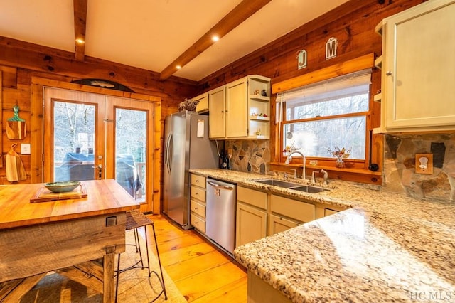 kitchen with sink, beamed ceiling, stainless steel appliances, light stone countertops, and light hardwood / wood-style floors