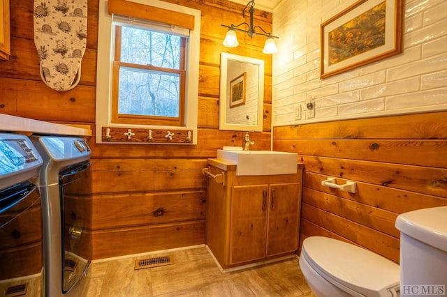 bathroom featuring independent washer and dryer, vanity, toilet, and wooden walls