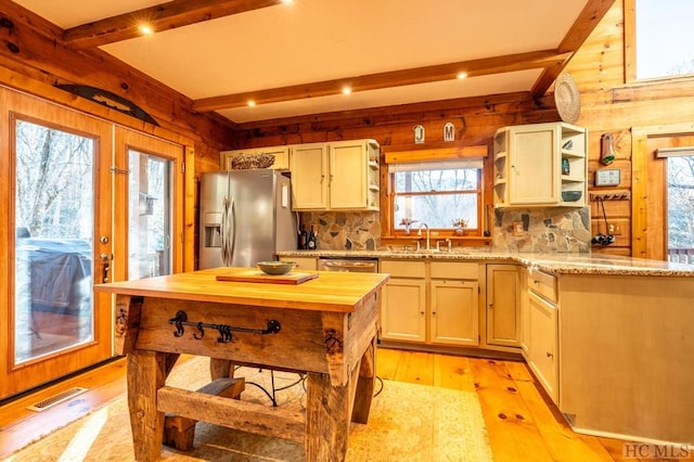 kitchen with beam ceiling, appliances with stainless steel finishes, wooden walls, and light hardwood / wood-style flooring