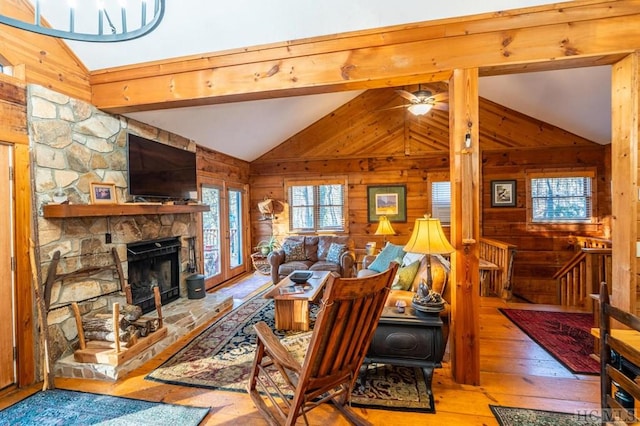 living room with vaulted ceiling with beams, ceiling fan, light hardwood / wood-style floors, wood walls, and a fireplace