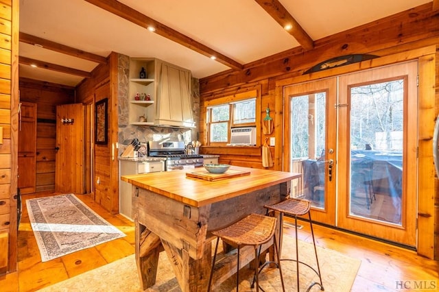 kitchen with stainless steel gas range, wooden counters, a center island, light hardwood / wood-style flooring, and beam ceiling