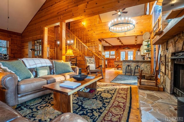 living room with a fireplace, ceiling fan with notable chandelier, wooden walls, and high vaulted ceiling