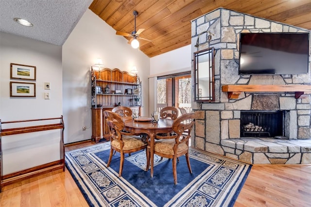 dining area featuring lofted ceiling, a stone fireplace, wooden ceiling, wood finished floors, and baseboards