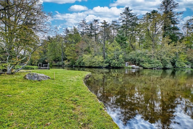 view of green lawn featuring a water view and a wooded view