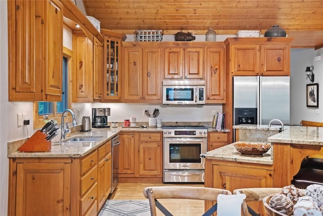 kitchen with glass insert cabinets, light stone countertops, appliances with stainless steel finishes, and a sink