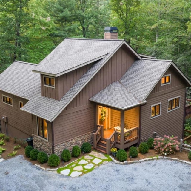 rustic home featuring a porch, a shingled roof, stone siding, board and batten siding, and a chimney