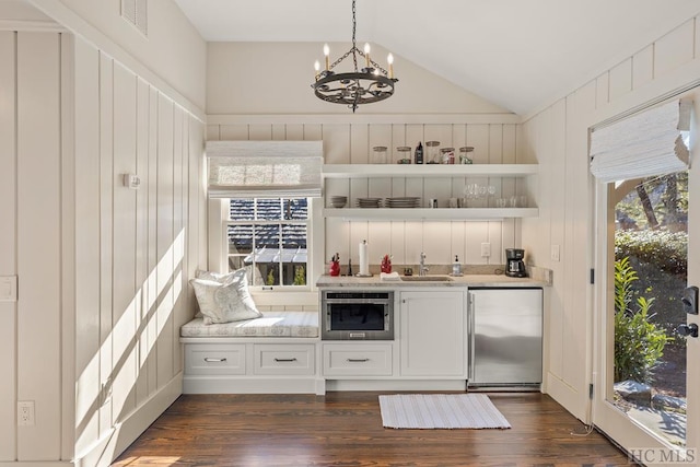 bar with lofted ceiling, white cabinetry, hanging light fixtures, appliances with stainless steel finishes, and wooden walls