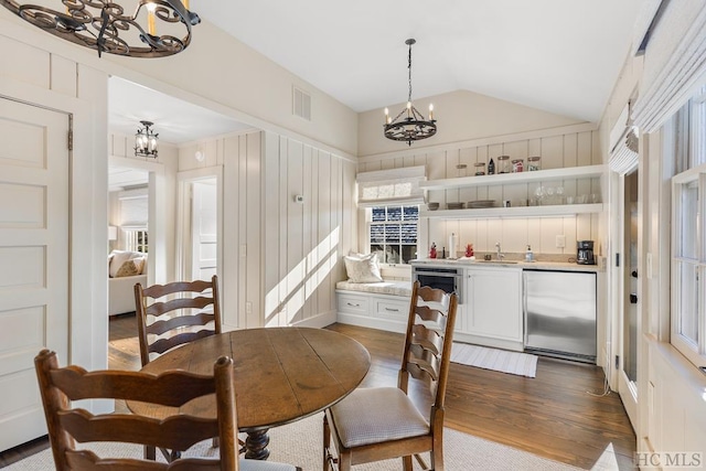 dining room featuring dark wood-type flooring, a healthy amount of sunlight, lofted ceiling, and a notable chandelier