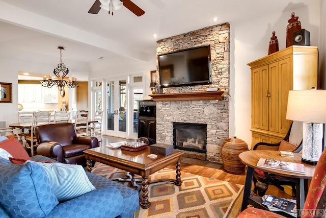 living room with ceiling fan with notable chandelier, light hardwood / wood-style flooring, and a stone fireplace