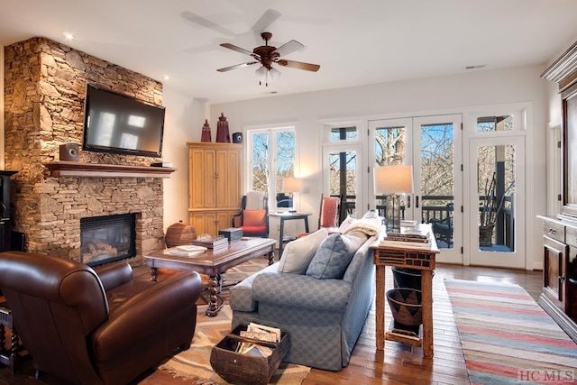 living room featuring a stone fireplace, a wealth of natural light, ceiling fan, and light hardwood / wood-style flooring