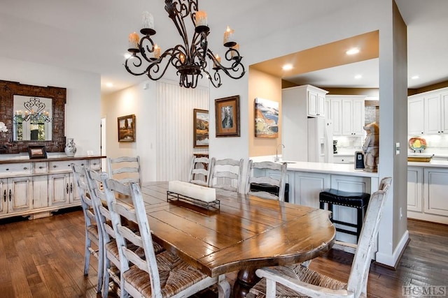 dining space with sink, dark wood-type flooring, and an inviting chandelier