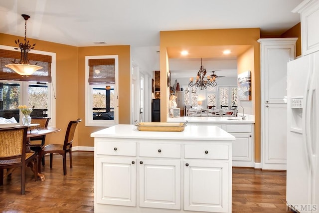 kitchen featuring white fridge with ice dispenser, decorative light fixtures, sink, dark wood-type flooring, and white cabinets